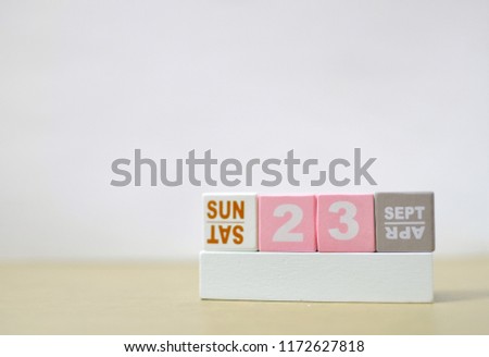 Sunday 23th September, Soft selective focus on pink wooden block calendar on burred wooden table with white cement background, copy space for text or wording.