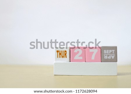 Thursday 27th September, Soft selective focus on pink wooden block calendar on burred wooden table with white cement background, copy space for text or wording.