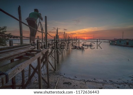 Young unidentified teenager taking outdoor pictures of sunset at old wooden jetty
