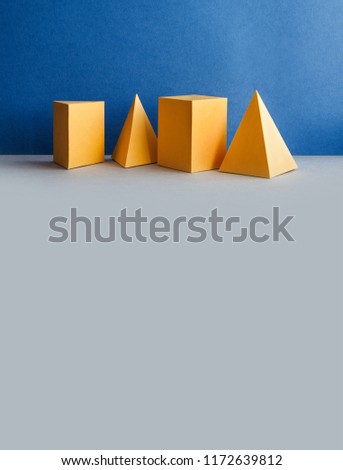 Three-dimensional pyramid tetrahedron cube rectangular objects on blue gray background. Abstract geometric figures. Yellow color Platonic solids still life background. copy space.