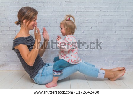 the girl, the mother and child in front of a white brick wall playing Patty-cake and kiss