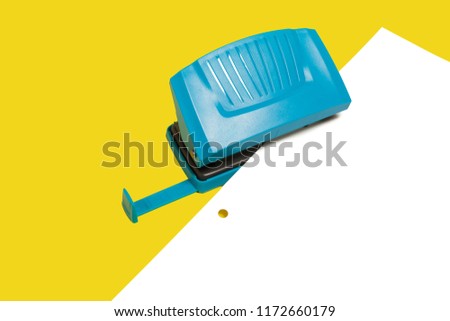 Blue plastic modern new office hole puncher lying with a paper isolated on a yellow background. free copyspace Royalty-Free Stock Photo #1172660179