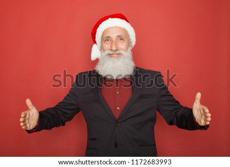 attractive business man in santa hat showing blank copy space above palm hand for client to add christmas product, present, gift, greeting and wishes text, looking happy and excited isolated on red.