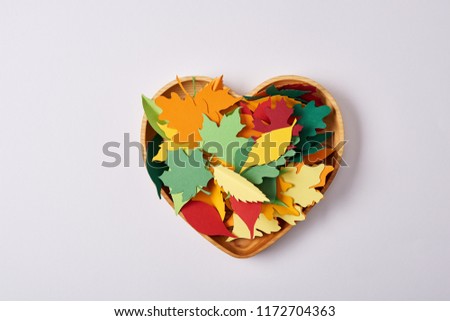 top view of wooden heart shaped box and colorful handcrafted leaves on white surface