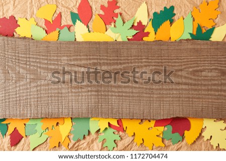 top view of wooden plank and colorful paper leaves arrangement on crumpled paper backdrop