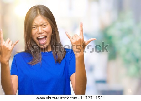 Young asian woman over isolated background shouting with crazy expression doing rock symbol with hands up. Music star. Heavy concept.