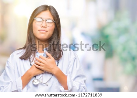 Young asian doctor woman over isolated background smiling with hands on chest with closed eyes and grateful gesture on face. Health concept.