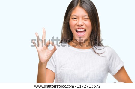Young asian woman holding football soccer ball over isolated background doing ok sign with fingers, excellent symbol