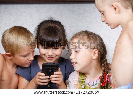 Children play on the mobile phone in games, an enthusiastic group of friends watch a cartoon on a tablet