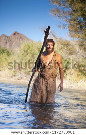 White Male Dressed as Jesus in Jewish Attire. Others as John the Baptist/ Prophet with burlap clothes and wood staff near river. Royalty-Free Stock Photo #1172733901