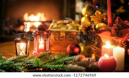 Closeup photo of golden gift box, candles and lanterns against Christmas tree and fireplace