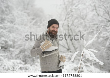 Bearded man with skates in snowy forest. Man in thermal jacket, beard warm in winter. Temperature, freezing, cold snap, snowfall. skincare and beard care in winter. Winter sport and rest, Christmas.