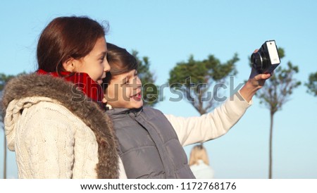 The children are on the street. The boy is holding a camera. The girl is showing a thumbs up. They make selfies