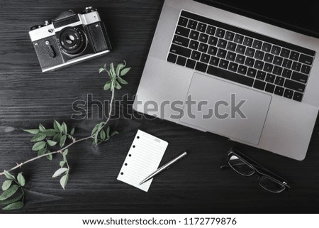 Laptop, photo camera, eyeglasses, rose branch and cup of coffee with white sheet on wooden table. Top view