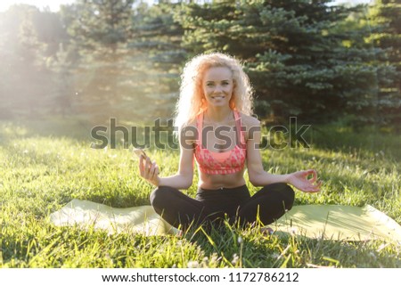 Image of young curly-haired sports woman practicing yoga on rug in park
