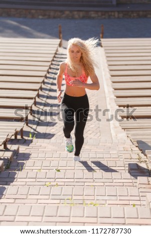 Photo of curly-haired athletic woman running through park among benches