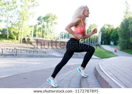Photo of curly-haired athletic woman running through park among benches