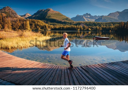 Alone male runner running in beautiful autumn morning nature by lake. Beautiful big mountains in background. Sport photo, edit space. high Tatras, Slovakia