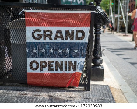 A makeshift grand opening sign hanging outside storefront on street