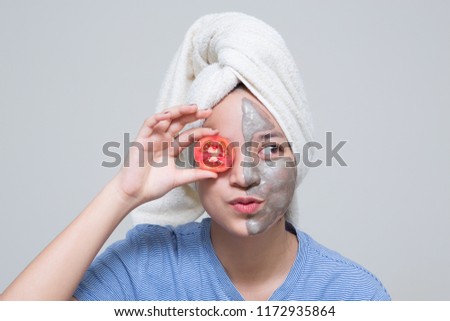 Beauty shot of Asian cute girl with beautiful skin shows mask cream on her face and holding tomato or cucumber as nutrient for treatment her facial skin Royalty-Free Stock Photo #1172935864