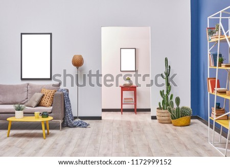 White blue wall concept living room style. Grey sofa and frame decoration. working table in the back and yellow bookshelf.