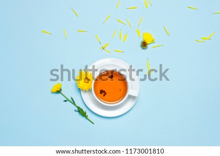 
Cup of herbal tea with a yellow chrysanthemum on blue background top view flat lay. Concept Good morning, Greeting card, floral background, still life with tea cup