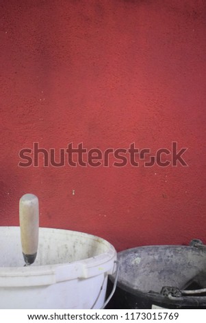 White and black bucket with spade inside in front of old red painted wall