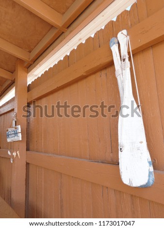 Decorative white wooden oars hanging on brown fence with welcome sign in distance