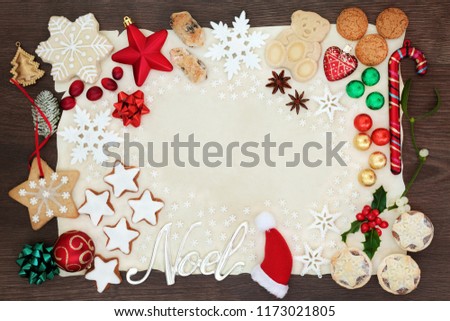 Noel and Christmas background border with silver sign and tree decorations, snowflakes, biscuits, cakes, chocolates and winter flora on parchment paper on rustic oak. Flat lay.