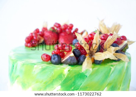 Cake with whipped green cream, decorated with fresh strawberries, blueberries, figs and physalis on white background. Picture for a menu or a confectionery catalog.