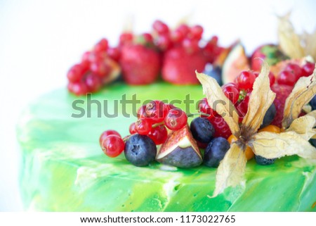 Cake with whipped green cream, decorated with fresh strawberries, blueberries, figs and physalis on white background. Picture for a menu or a confectionery catalog. Close up.
