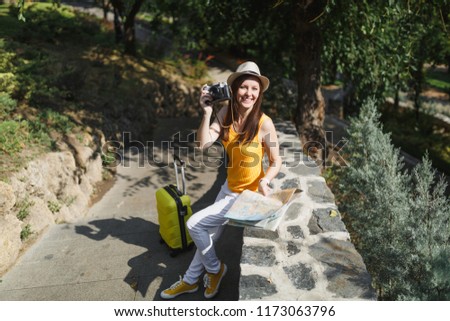 Happy traveler tourist woman in hat with suitcase, city map take pictures on retro vintage photo camera in city outdoor. Girl traveling abroad to travel on weekends getaway. Tourism journey lifestyle