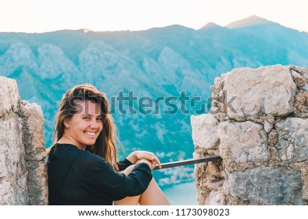 young adult woman sitting on top of hill on sunset with beautiful view of kotor.