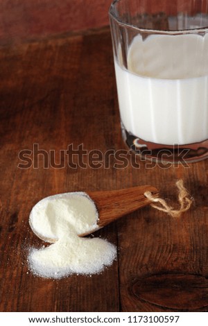 Spoon with milk powder, glass with milk over wooden background