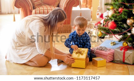 Little boy with mother sitting under Christmas tree and open gift box