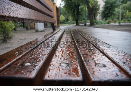 A nice brown bench outdoors. The bench is wet after some rain in the street. Bright and colorful picture. A beautiful place to relax. 