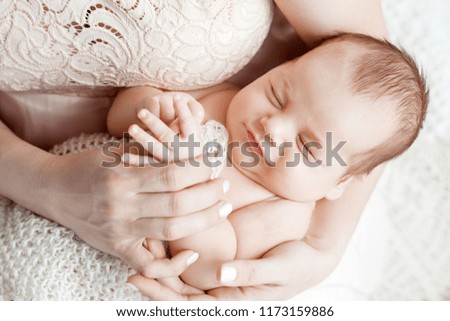 Loving baby sleeping in mother's hands. Closeup picture. Happy mother and her slipping smilibg newborn baby in the bed