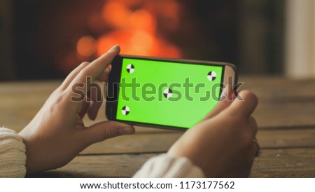 Closeup photo of young woman holding smartphone and making image of burning fireplace. Empty green screen for inserting your own picture or text
