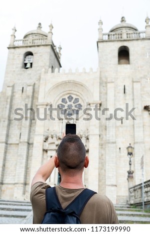 closeup of a young caucasian man, seen from behind, taking a picture of the Porto Cathedral, in Porto, Portugal, with his smartphone
