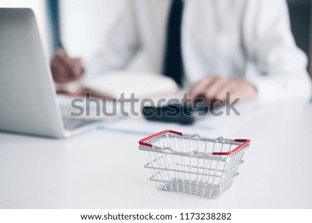 Small Shopping cart or shopping basket and laptop on the desk in ecommerce office,Online shopping concept.