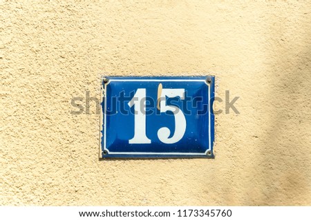 Old vintage house address metal plate number 15 fifteen on the plaster facade of abandoned home exterior wall on the street side