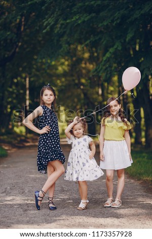 Little beautiful girls in beautiful dresses are walking in the summer park with balloons in their hands