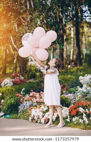 Little beautiful gir in beautiful dress in the summer park with balloons in hands