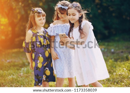 Little beautiful gir in beautiful dress are walking in the summer park with phone