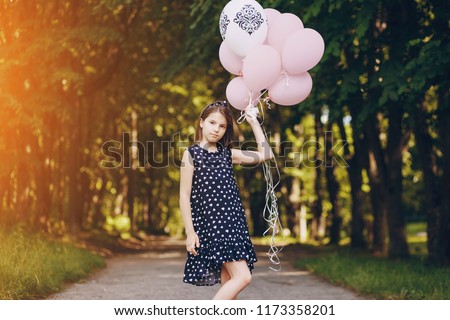Little beautiful gir in beautiful dresses are walking in the summer park with balloons in a  hands
