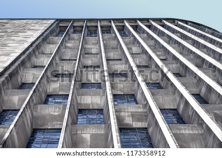 Tall grey wall of a cathedral beneath the blue sky. With blue translucent windows  that form part of an interesting pattern. 