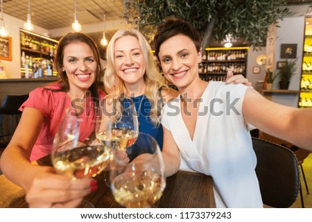 people, technology and lifestyle concept - women drinking wine and taking selfie at bar or restaurant