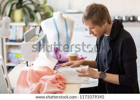 people, clothing and tailoring concept - fashion designer reading book at studio