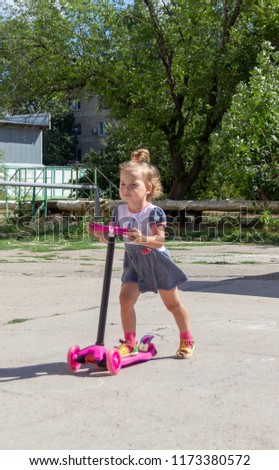 Cute child skilfully skates on a pink two-wheeled scooter on a summer sunny day
