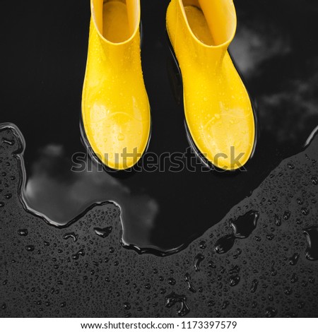 Yellow rubber boots stand in a puddle in which the clouds are reflected. Black background, top view.